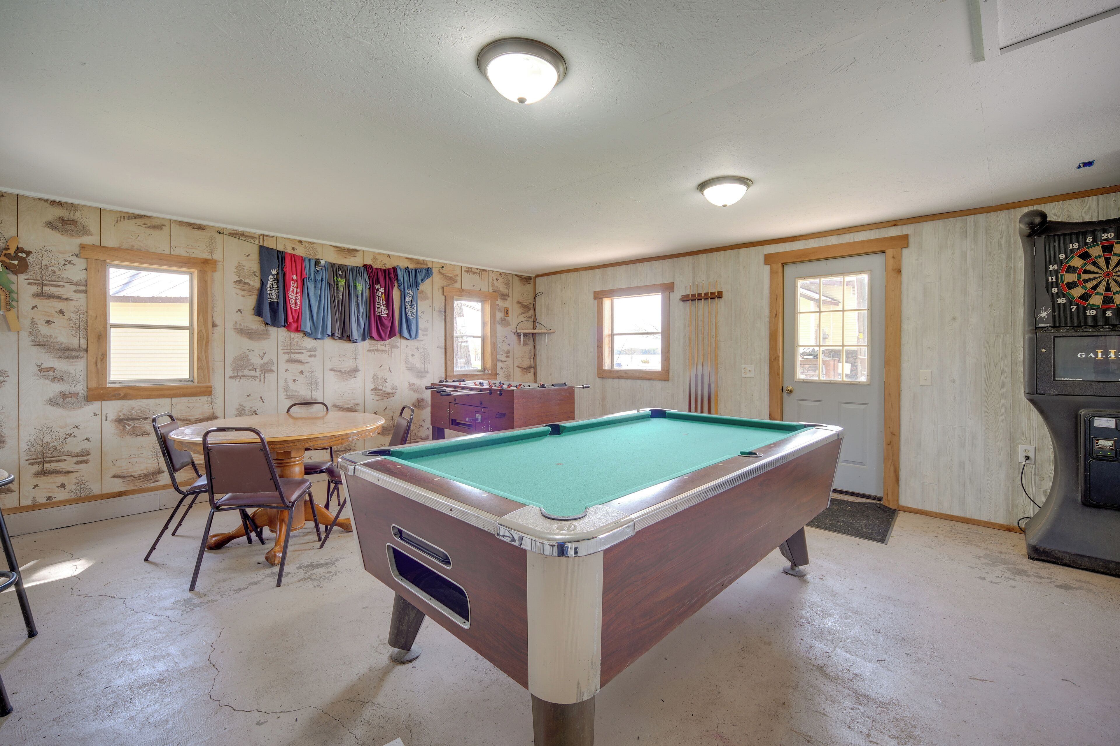 A pool table in a room with wooden walls and windows.