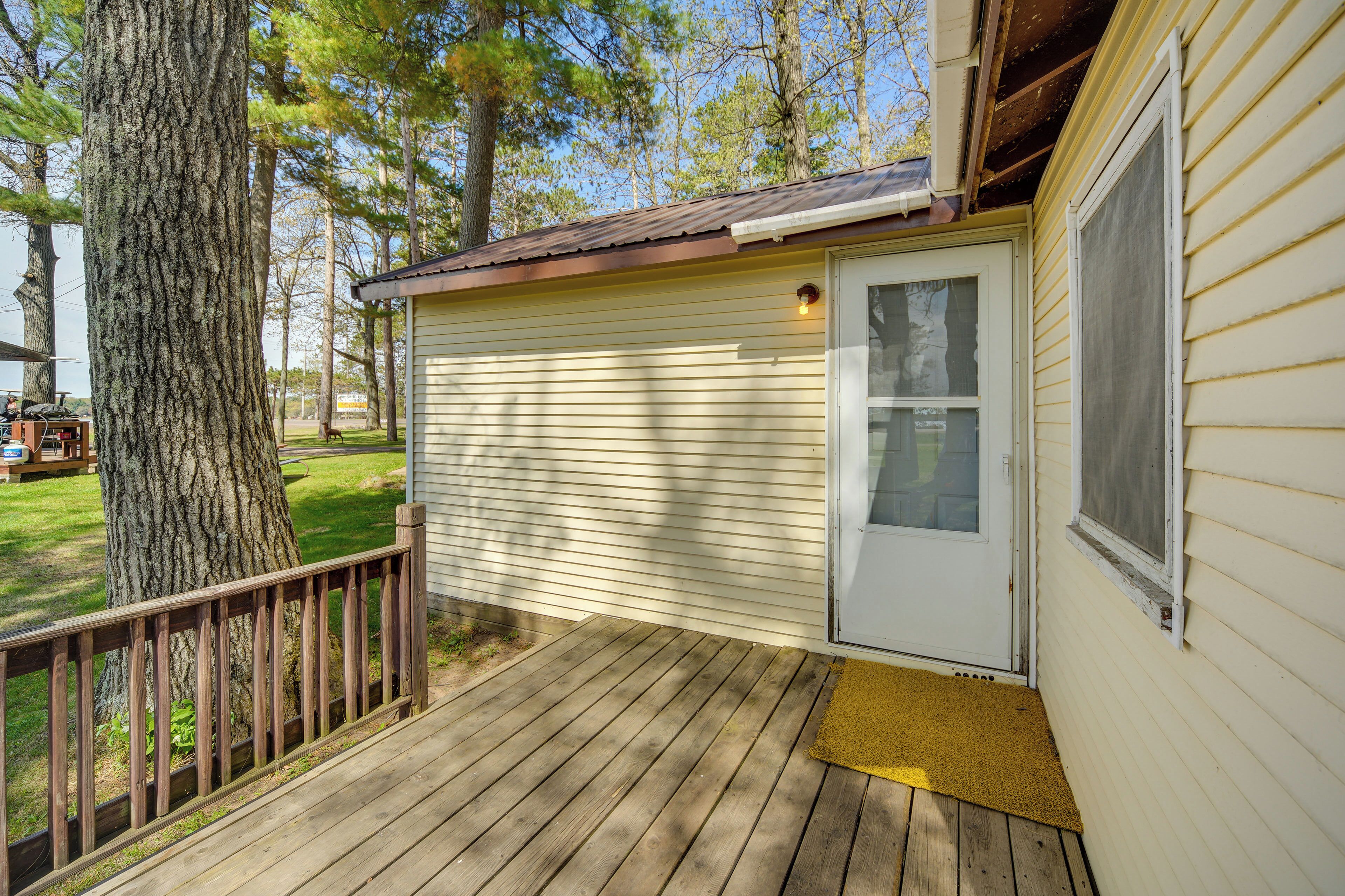 A wooden deck with a door and window, surrounded by trees.