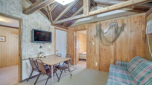 Een kamer met een houten plafond, een aan de muur bevestigde televisie, een eettafel met stoelen en een gestreepte bank.