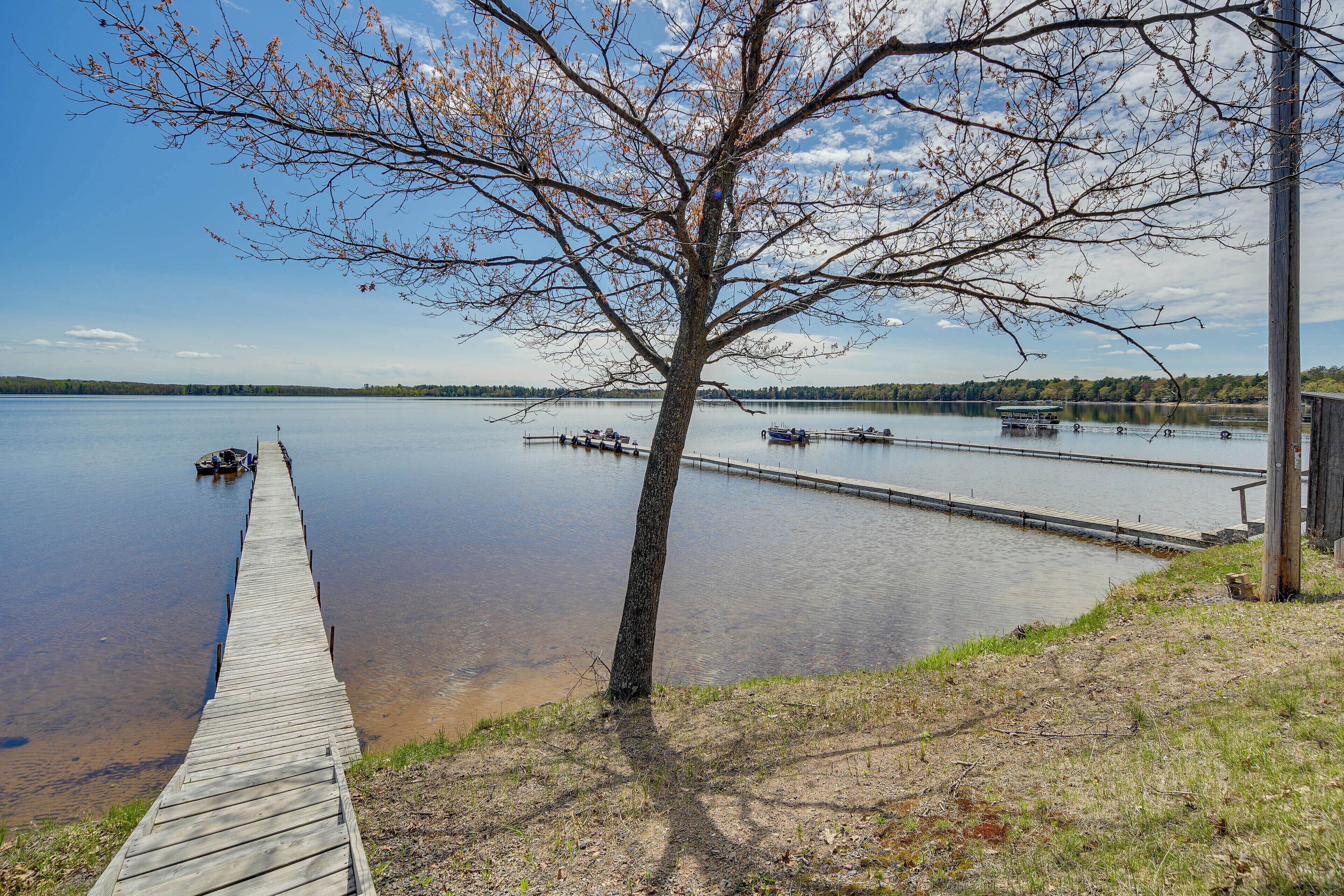 A wooden dock extending into a calm lake with boats docked nearby and a tree in the foreground.