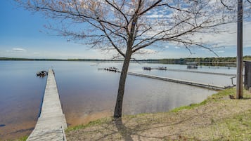 A wooden dock extending into a calm lake with boats docked nearby and a tree in the foreground.