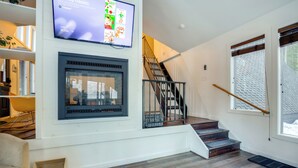 A modern living room with a fireplace, a staircase, and a television mounted on the wall. - Near Trails & Breweries: Cabin w/ Hot Tub in Breck (Breckenridge)
