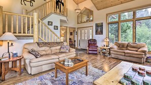 A spacious living room with a wooden staircase, two sofas, a coffee table, and a large window offering a view of the outdoors.