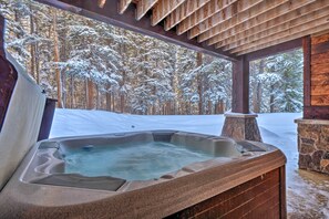 A hot tub in a wooden cabin with a snowy forest view.