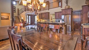 A spacious dining area with a large wooden table and chairs, a chandelier, and a kitchen with wooden cabinets and stainless steel appliances. - Blue River Home w/ Hot Tub, 6 Mi to Skiing! (Breckenridge)