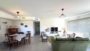 Ein geräumiger Wohnbereich mit Esstisch, Stühlen, einer Couch, einem Fernseher und einer Küchenzeile.