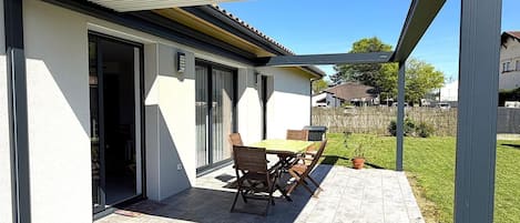 Un patio techado con una mesa y sillas, una puerta corrediza de vidrio y vistas a una zona residencial.