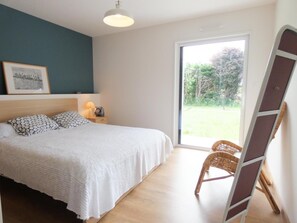 A bedroom with a bed, bedside table with lamp, framed picture, and a view of the outdoors. - Le Gîte de la Battère (SAUBUSSE)