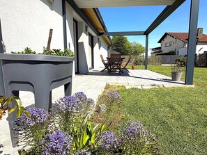 Une terrasse couverte avec une table et des chaises, une pelouse verdoyante et un bâtiment en arrière-plan.