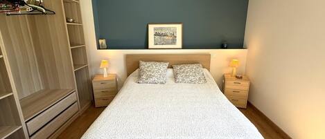 A bedroom with a bed, two bedside tables, a wardrobe, a framed picture on the wall, and a ceiling light.