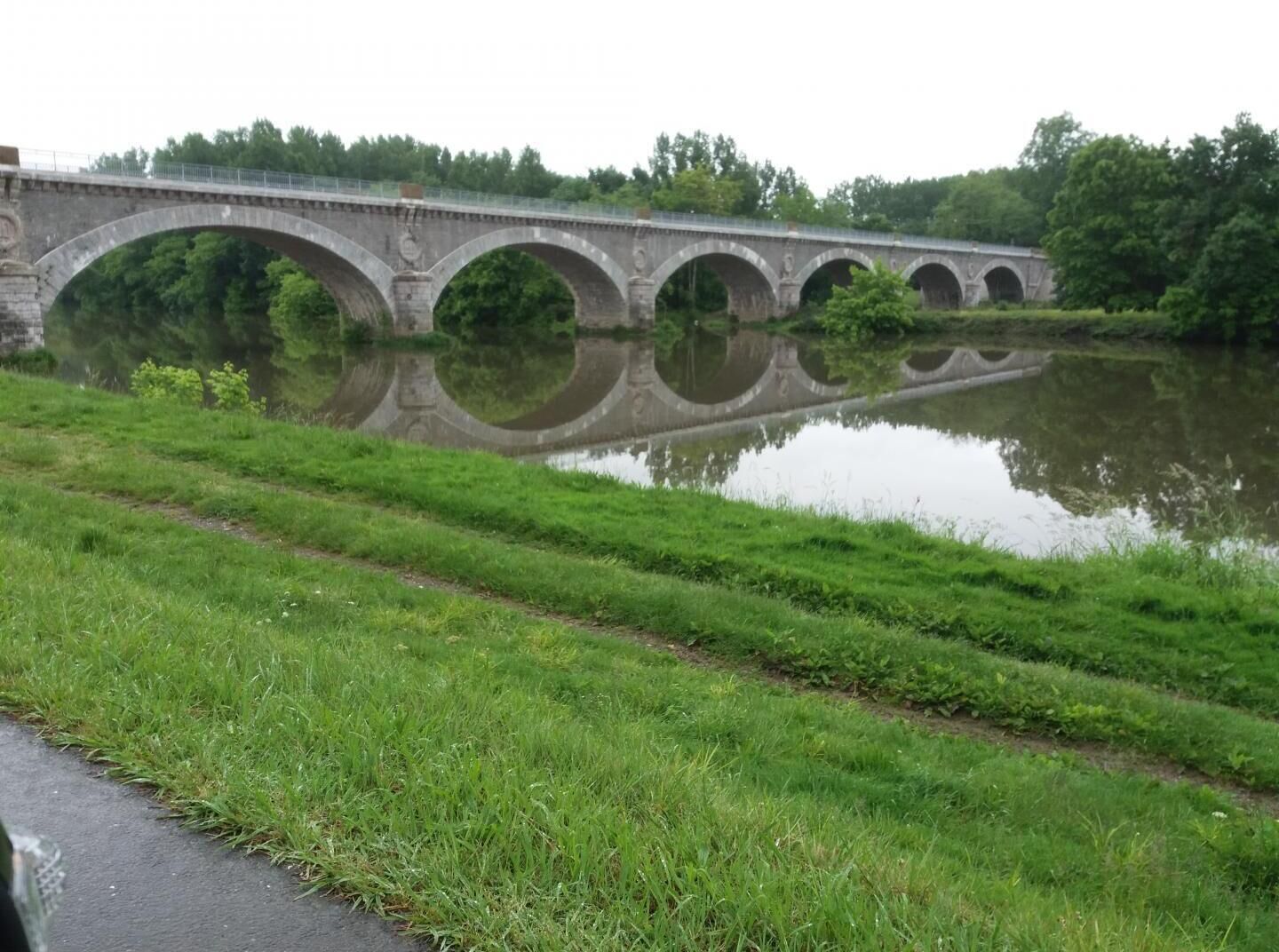 A stone bridge with multiple arches over a calm river, surrounded by lush greenery.