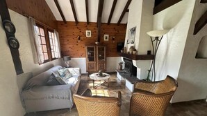 Un salon chaleureux avec un plafond en bois, un canapé, des fauteuils en osier, une cheminée et un buffet.