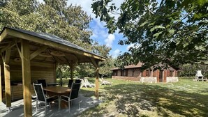 Un espace extérieur abrité, avec une table et des chaises, un bâtiment en briques en arrière-plan et une pelouse verdoyante.