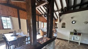 Un intérieur rustique avec des poutres apparentes, un banc en pierre, un sol carrelé et un coin repas comprenant une table et des chaises.
