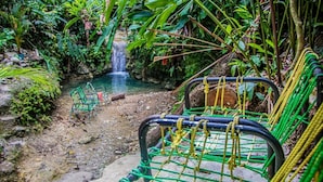 Eine natürliche Umgebung mit einem kleinen Wasserfall, grünen Stühlen und einer Hängebrücke.