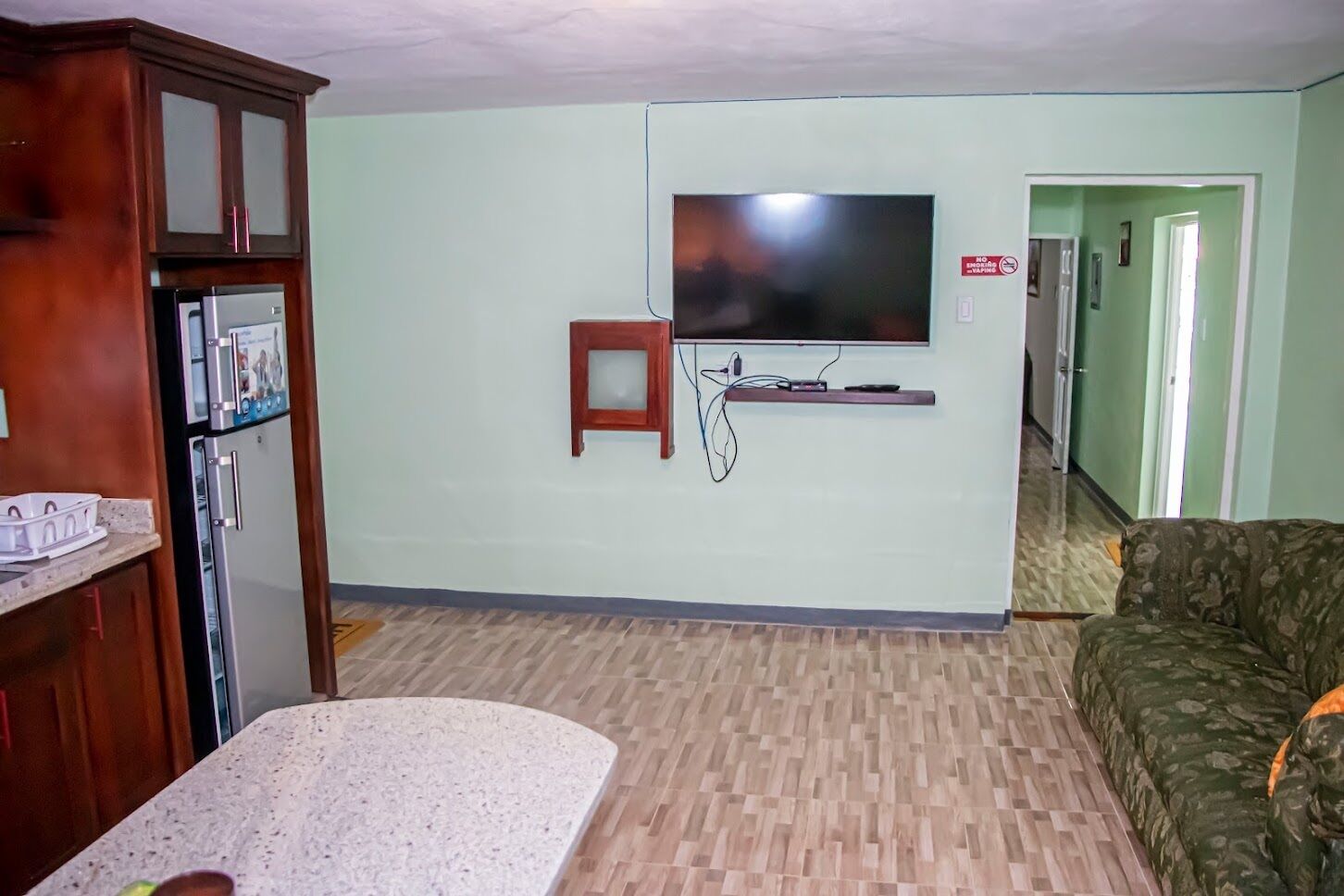 Una sala de estar con un televisor montado en la pared, un mueble de madera, un taburete pequeño y un sofá.