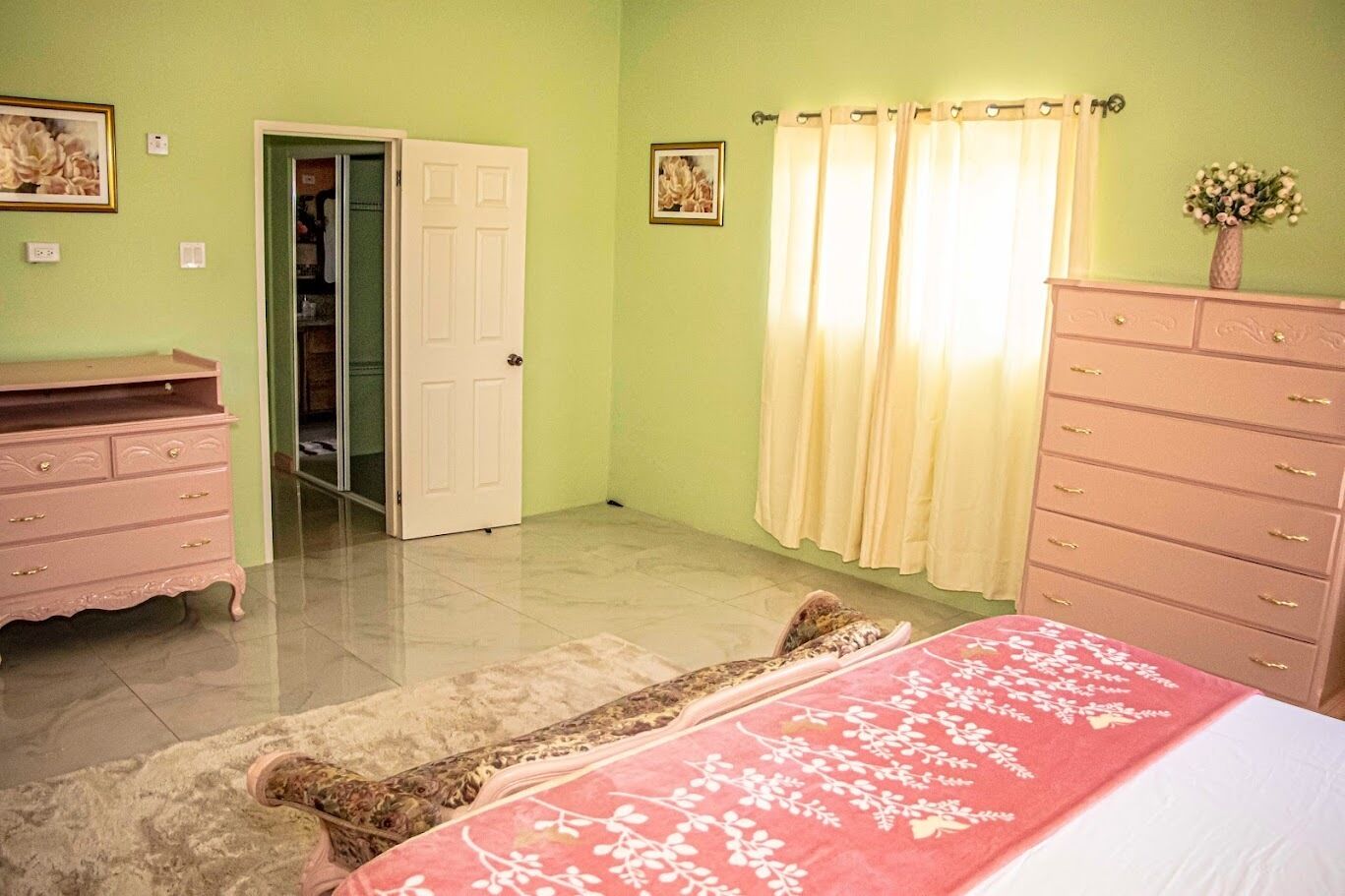 A bedroom with a bed, a dresser, a wardrobe, a door, and a window with curtains.
