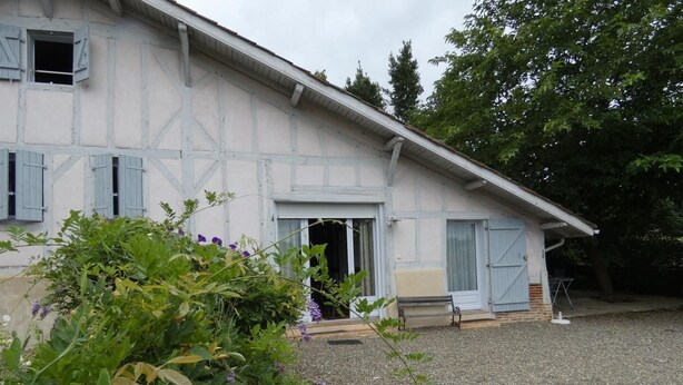 Une maison à deux étages avec une allée en gravier et un jardin où poussent différentes plantes et fleurs.