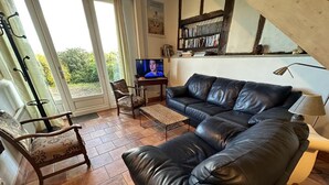 Un salon avec un canapé en cuir noir, une chaise en bois, une petite table et un téléviseur.
