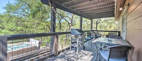 A covered outdoor deck with a grill, dining table, and chairs, overlooking a swimming pool.