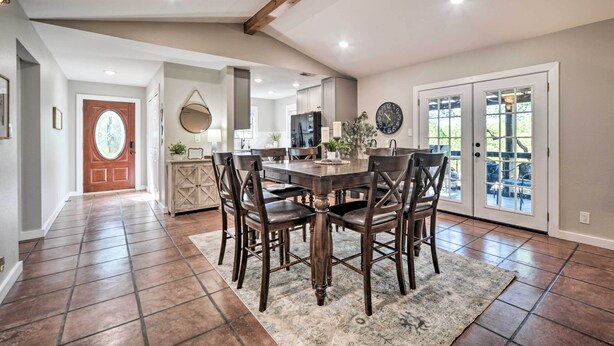 A spacious dining area with a wooden table and chairs, a kitchen in the background, and a large clock on the wall.