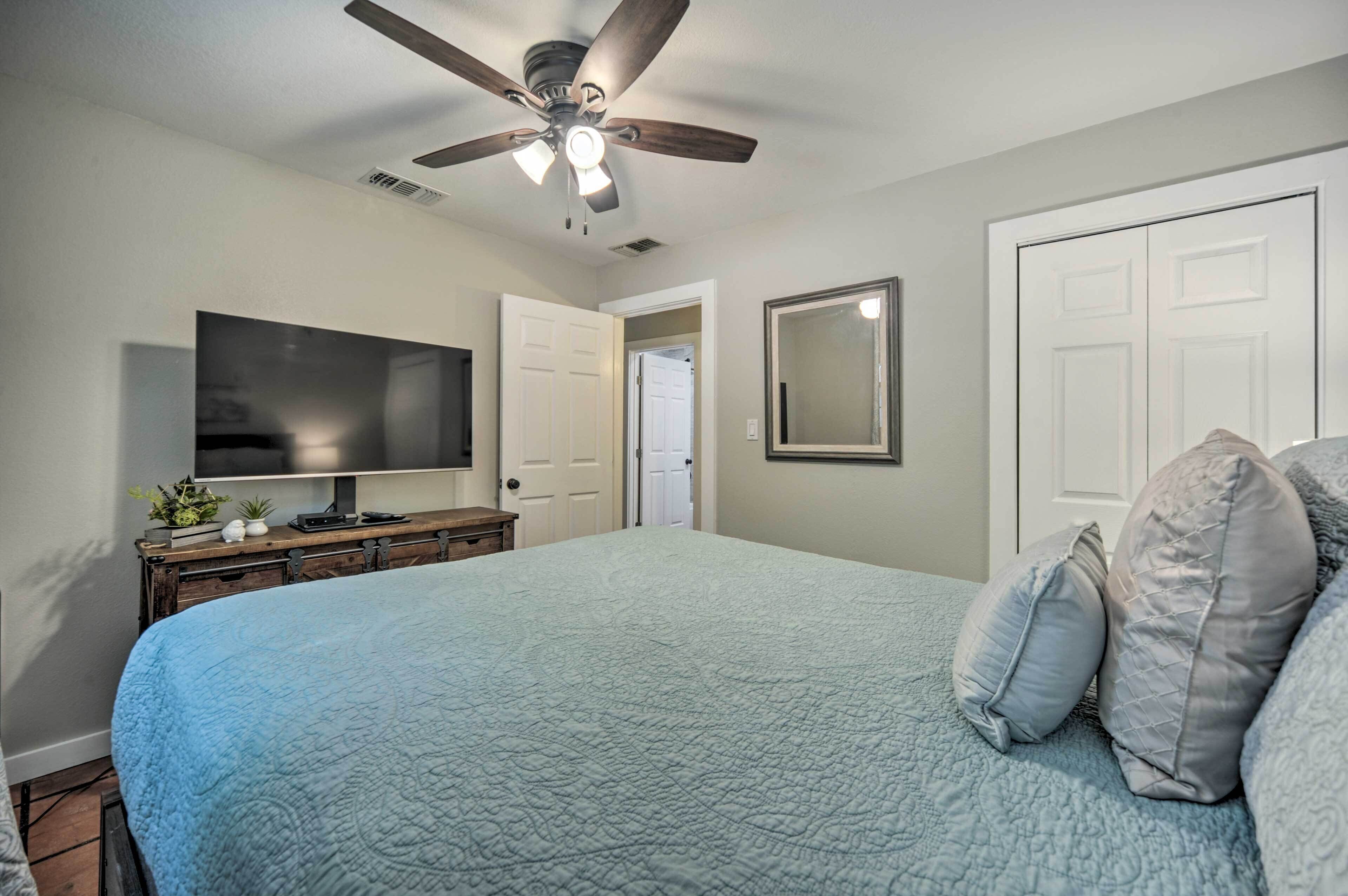 Un dormitorio con cama, ventilador de techo, televisor, cómoda y una puerta.