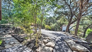 A stone pathway leading through a wooded area with a small building in the background.