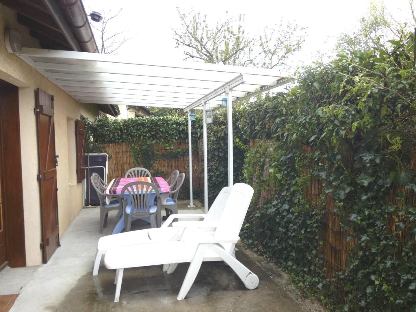 A covered patio area with a table and chairs, a white lounge chair, and a wooden fence.