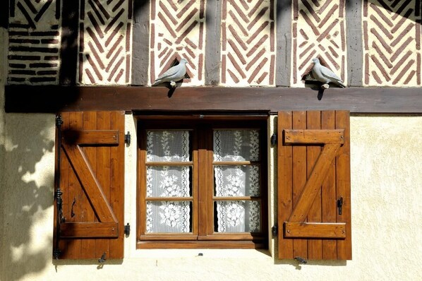 A traditional building with a window featuring wooden shutters and lace curtains.