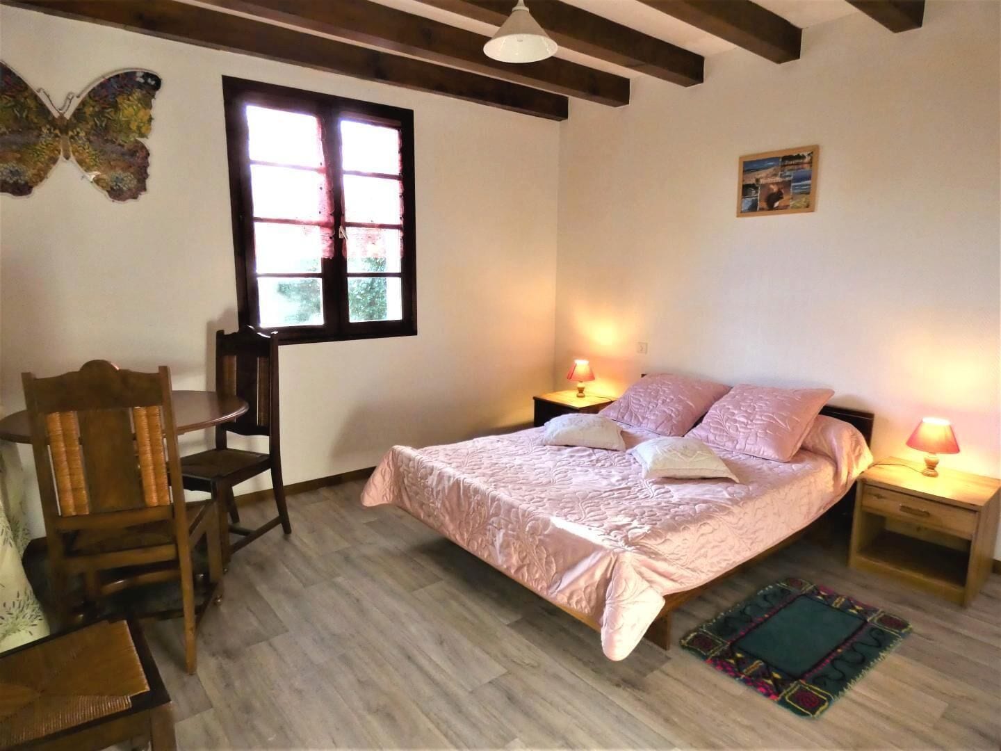Een slaapkamer met een bed, twee nachtkastjes, een stoel, een raam en een decoratie aan de muur.