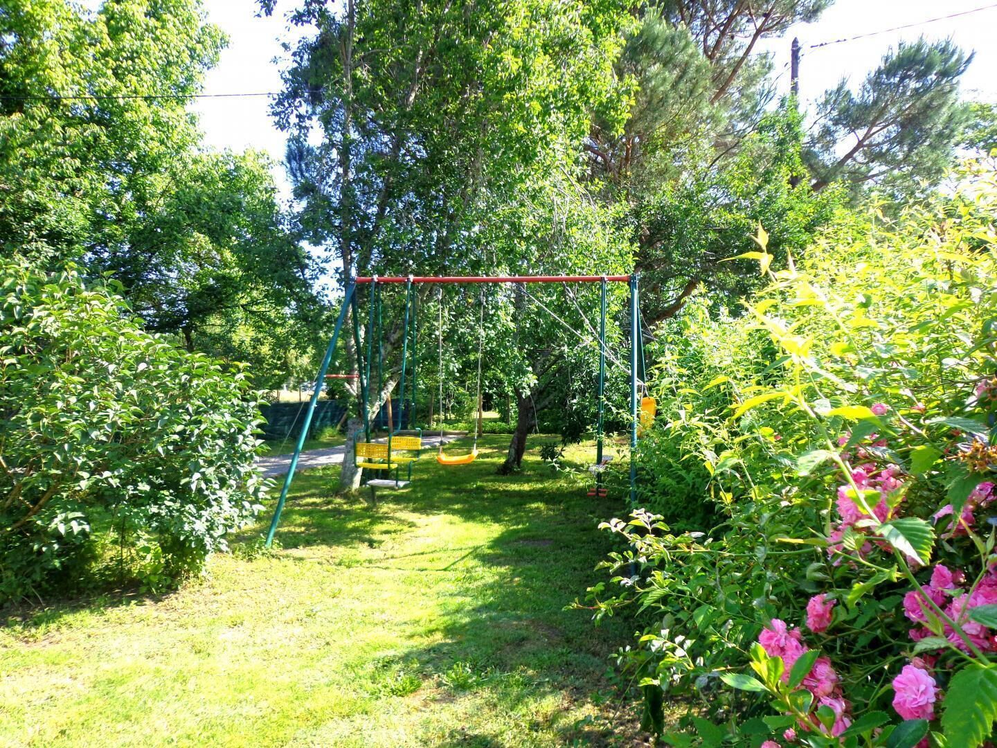 Um jardim com baloiço, rodeado por vegetação exuberante e plantas floridas.