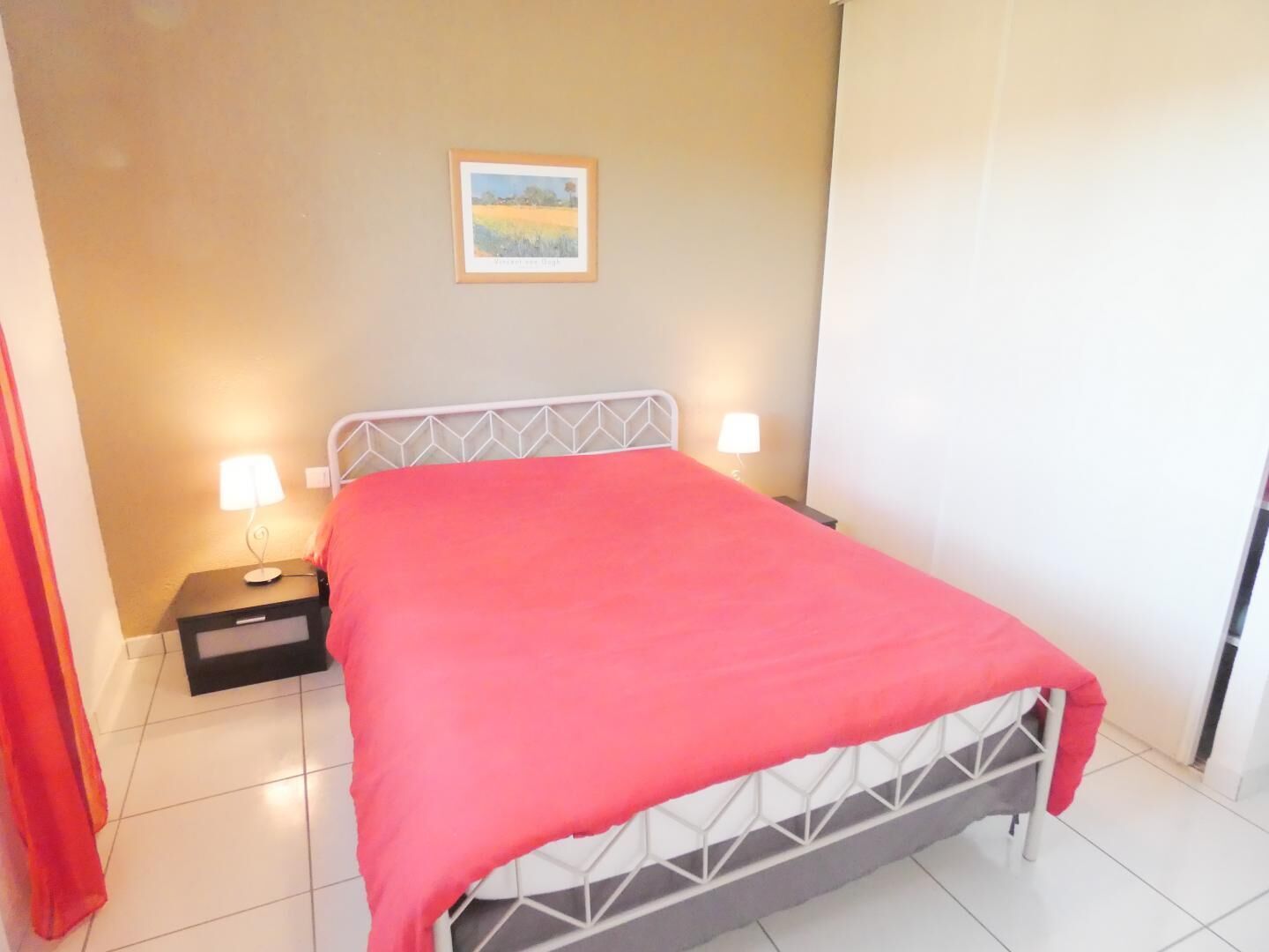 A bedroom with a bed, two bedside tables, a nightstand, a wall-mounted picture, and a door.