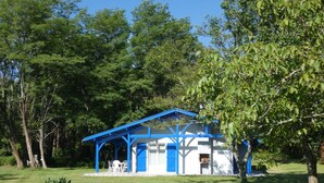 A small, single-story building with a blue roof and white walls, surrounded by trees and grass. - Gîte de Deze - Herm - Gîte (HERM)
