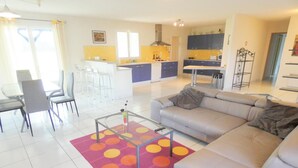 A modern living room with a sofa, a coffee table, and a dining area with chairs. - Gîte de Deze - Herm - Gîte (HERM)