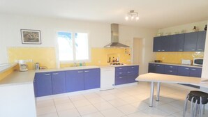 A modern kitchen with white cabinets, a central island, and a dining area with a table and chairs. - Gîte de Deze - Herm - Gîte (HERM)