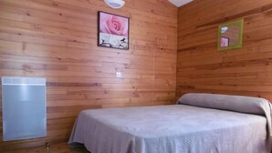 A wooden-paneled room with a bed, a wall-mounted heater, and a framed picture of flowers.