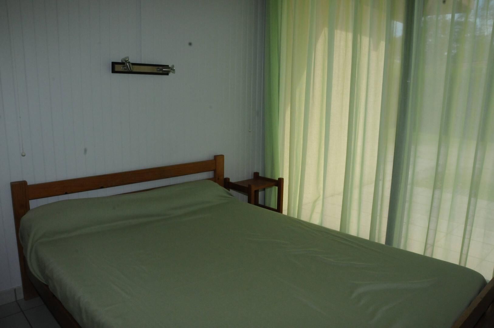 Une pièce simple, avec un lit, une petite table et un rideau.