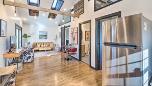 A modern kitchen with a stainless steel refrigerator, wooden flooring, and a loft-style ceiling with skylights.