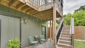 A wooden deck with a staircase leading to a second level, outdoor seating area with chairs and a table, and a potted plant.
