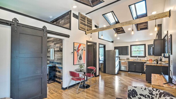 A spacious living area with a large sliding door, a dining table with red chairs, a sofa with a cowhide pattern, and a kitchen area with a large island and modern appliances.