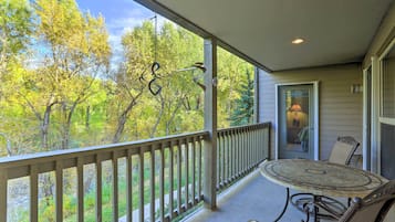 A covered porch with a table and chairs, a railing, and a view of trees.