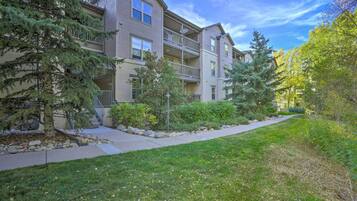 A multi-story residential building with a landscaped front yard, a pathway, and mature trees.