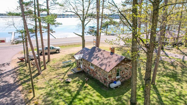A rustic cabin with a stone exterior, a metal roof, and a small attached shed, surrounded by trees and a lake view. - Convenient Cabin w/ Access to 3 Boat Docks! (Stone Lake)