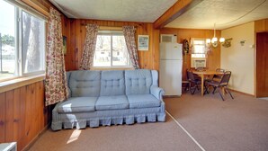 A room with a sofa, a dining table with chairs, a refrigerator, and a window with curtains. - Convenient Cabin w/ Access to 3 Boat Docks! (Stone Lake)