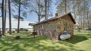 A stone cabin with a chimney, surrounded by trees and a grassy area. - Convenient Cabin w/ Access to 3 Boat Docks! (Stone Lake)