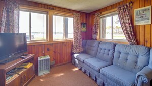 A cabin interior with a television, wooden walls, a sofa, and large windows. - Convenient Cabin w/ Access to 3 Boat Docks! (Stone Lake)