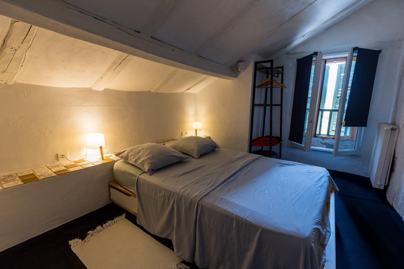 Une chambre à coucher avec un lit, des lampes de chevet, une fenêtre avec des rideaux et un radiateur.