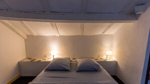 Une petite chambre avec un lit simple, deux lampes de chevet, des murs blancs et des poutres apparentes au plafond.