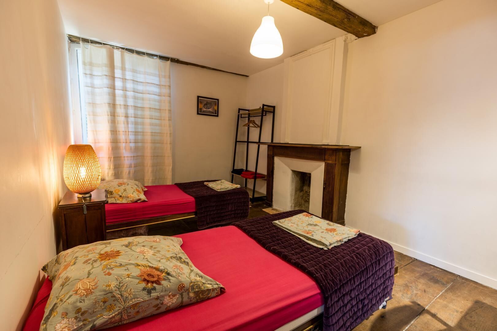 A room with two beds, a fireplace, a hanging chair, and a lamp.