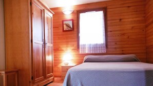 A wooden room with a bed, a wardrobe, a nightstand with a lamp, and a window with a curtain. - Les Genêts - Brocas - Gîte (BROCAS)